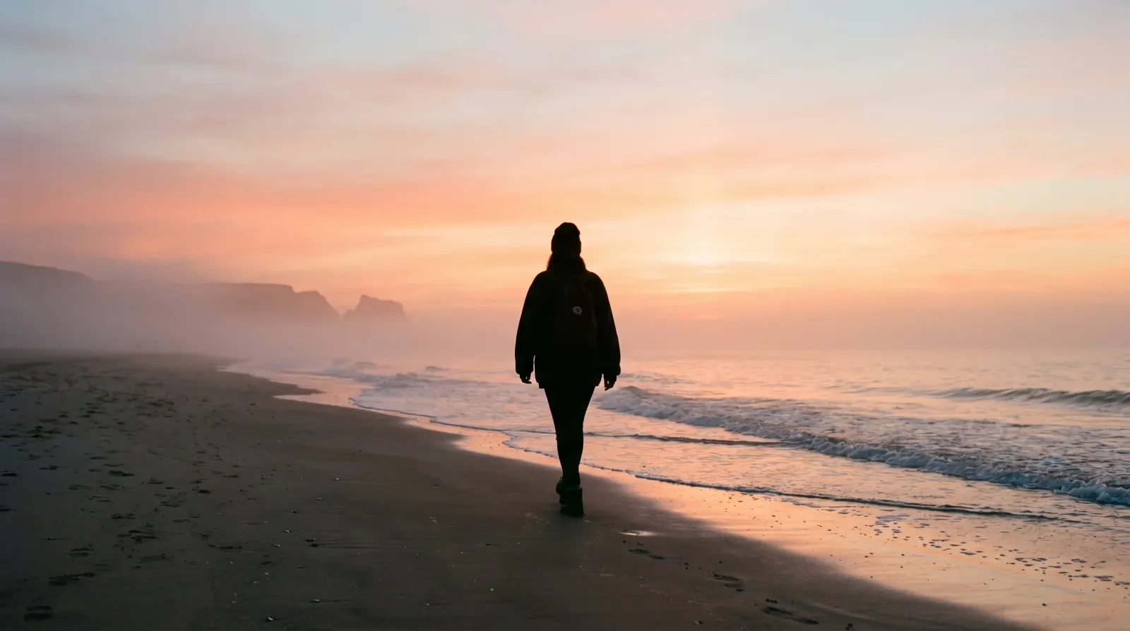 Siluett av person som promenerar vid havet i soluppgång
